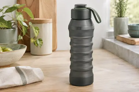 Bouteille filtrante sombre et compressible avec bouchon amovible et boucle en silicone sur une table claire.