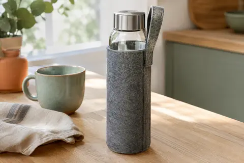 Gourde en verre borosilicaté avec couvercle inox et housse grise en feutre posée sur une table en bois
