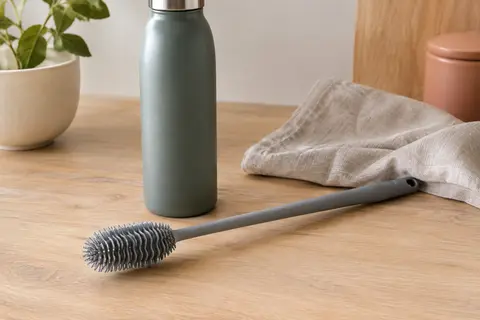 Goupillon gris en silicone à long manche posé près d’une gourde sur un plan de cuisine clair.