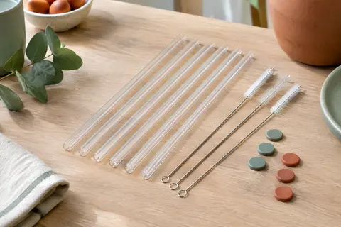 Six pailles transparentes réutilisables avec trois goupillons et des autocollants sur une table en bois clair.