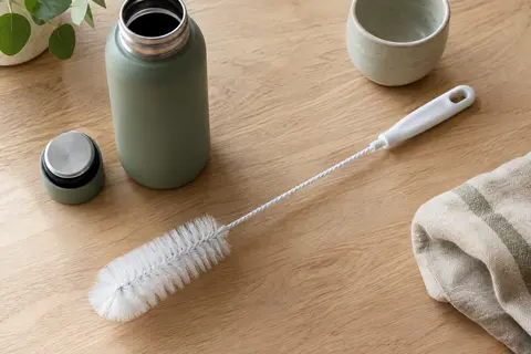 Goupillon blanc de 33 cm posé près d’une gourde ouverte sur un plan de travail en bois clair.