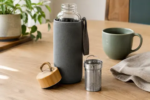 Bouteille en verre borosilicate avec housse grise, couvercle en bambou et sangle sur une table claire