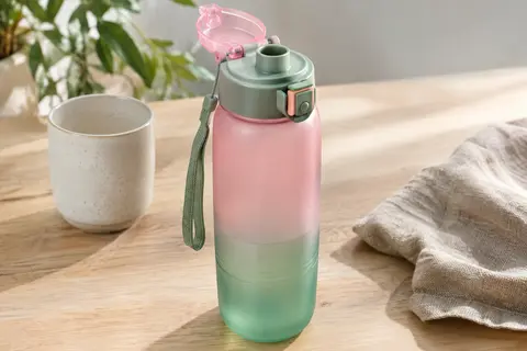 Gourde rose et verte en plastique givré avec couvercle rabattable et cordon, posée sur une table en bois clair.