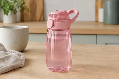 Gourde enfant Ion8 rose clair avec couvercle rabattable et boucle de transport, posée sur une table en bois clair.