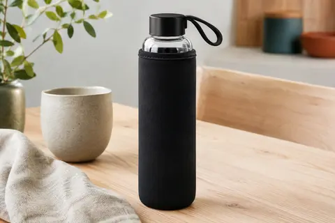 Bouteille en verre Nerthus avec housse noire en néoprène et boucle de transport, posée sur une table en bois clair.
