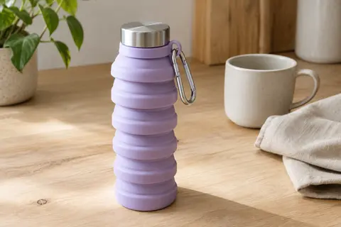 Gourde pliable en silicone lilas avec couvercle en acier inoxydable et mousqueton sur une table claire