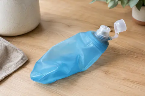 Flasque souple bleue de 150 ml avec valve à débit élevé et couvercle rabattable, posée sur une table.