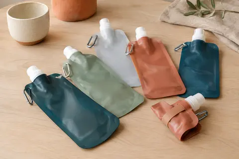 Lot de gourdes souples et pliables aux couleurs assorties, avec boucles métalliques sur une table en bois clair.