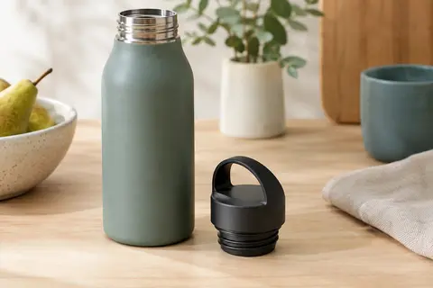 Bouchon de rechange noir à vis posé près du goulot étroit d’une gourde sur une table en bois clair.