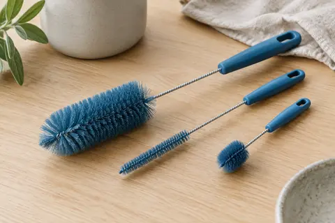 Trois brosses bleues pour gourde, paille et bec verseur posées sur un plan de travail en bois clair.