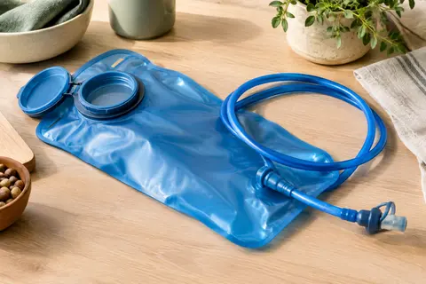 Poche d’hydratation bleue avec tuyau amovible et embout à valve, posée sur une table en bois clair.